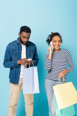 Şok olmuş Afrikalı Amerikalı bir adam akıllı telefondan mutlu bir eşin yanında mavi üzerine konuşuyor.