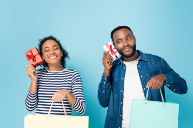 Neşeli Afrikalı Amerikalı karı koca alışveriş torbaları ve mavi kutular tutuyorlar.