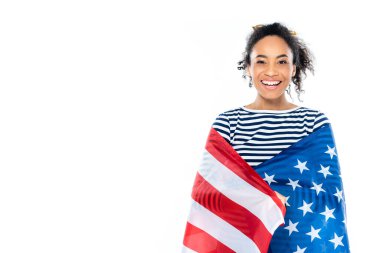 Amerika bayrağına sarılmış neşeli Afro-Amerikalı kadın, beyaz kameraya gülümsüyor.