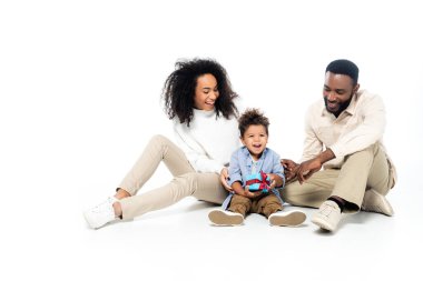 Mutlu Afrikalı Amerikalı ebeveynler oğlunun yanında beyaz hediye kutusuyla oturuyorlar.