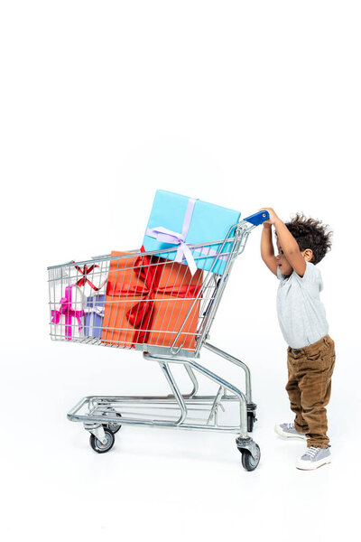 little african american child moving shopping cart with gift boxes on white