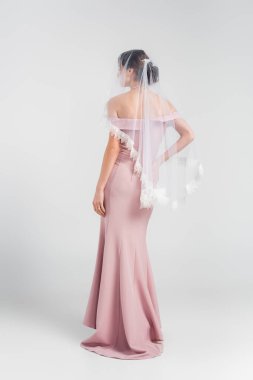 Pembe elbiseli ve peçeli gelinin gri üzerine poz verişi.