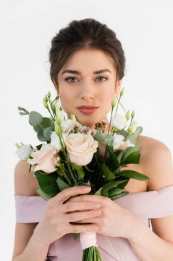 Düğün buketi takmış genç bir kadın beyaz kameraya bakıyor.