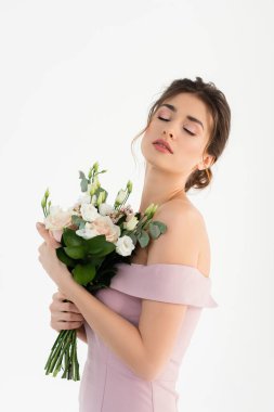 Büyüleyici bir kadın düğün buketini tutarken gözleri kapalı beyazların üzerinde dikiliyor.