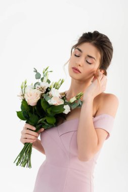 Şehvetli bir kadın, yüzün yanında el ele tutuşurken, beyaz bir buketle poz veriyor.