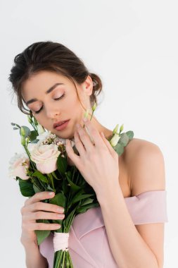 Büyüleyici bir kadın düğün buketini tutarken gözleri kapalı beyazların üzerinde dikiliyor.