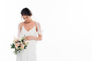 Gelinlik giymiş hamile bir kadın elinde beyaz bir buket tutuyor.