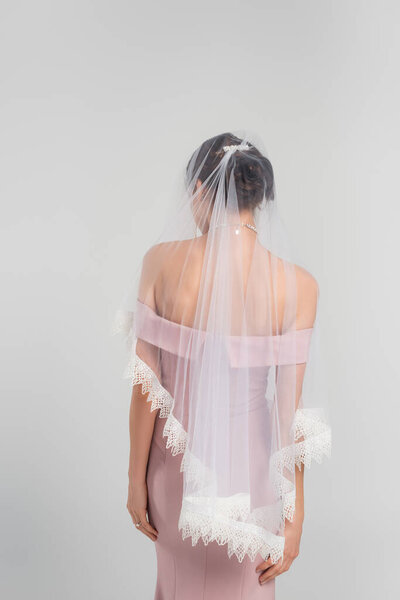 back view of young woman in pink dress and veil posing isolated on grey