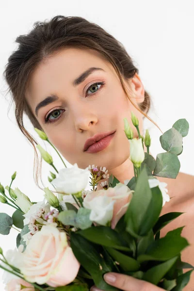 sensual woman with natural makeup looking at camera near wedding bouquet isolated on white