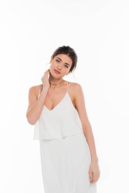 Gelinlik giymiş şehvetli bir kadın beyazlar içinde poz verirken boynuna dokunuyor.