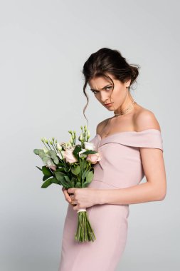 Kızgın nişanlı, gri renkte izole düğün buketini tutarken kameraya bakıyor.