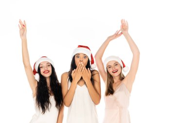 Genç ve neşeli ırklar arası kadınlar Noel Baba şapkaları ve elbiseleriyle beyazların üzerinde tek başlarına duruyorlar.