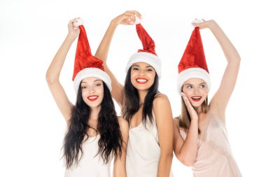 positive interracial women adjusting santa hats isolated on white clipart