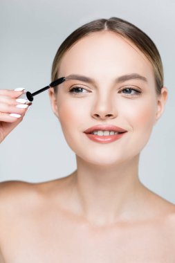 Çıplak omuzlu genç bir kadın maskara sürüyor. Gri renkte. 