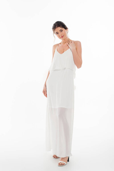 Вид в полный рост чувственной женщины в свадебном платье, улыбающейся перед камерой на белом