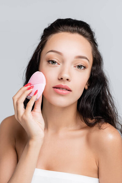 young woman using cleansing brush isolated on grey