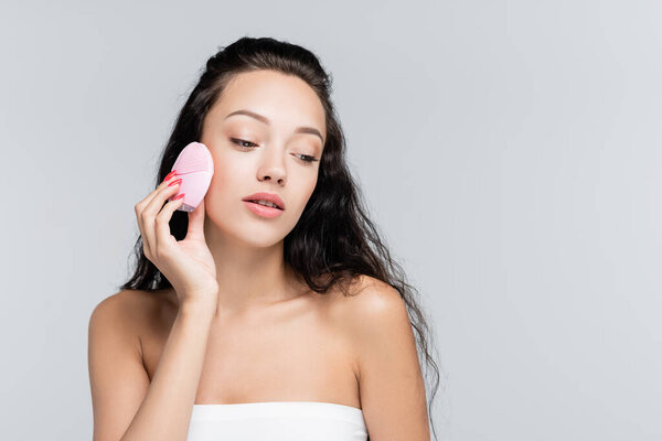brunette young woman using cleansing brush isolated on grey