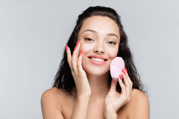 happy young woman using cleansing brush isolated on grey
