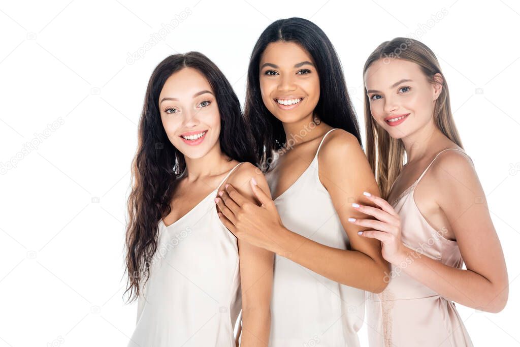 joyful interracial women in dresses smiling isolated on white