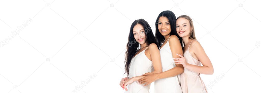 pleased interracial women in dresses smiling isolated on white, banner