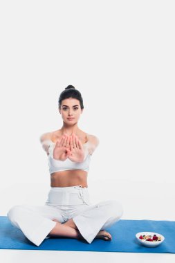 Yoga yapan kadın mısır gevreği kasesinin yanında poz veriyor. Beyaz arka planda spor minderinde böğürtlen var. 