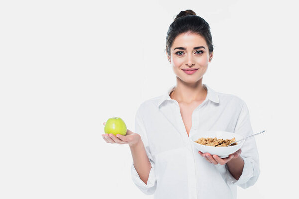 Smiling woman holding fresh apple and bowl of cereals isolated on white 