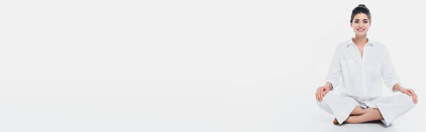 Веселая женщина улыбается в камеру, сидя в позе йоги на белом фоне, баннер 