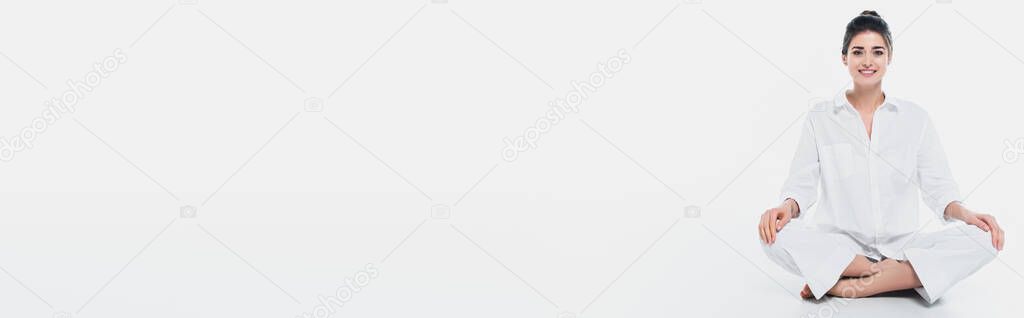 Cheerful woman smiling at camera while sitting in yoga pose on white background, banner 