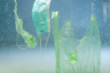 Tıbbi maskenin yanındaki plastik torbalar ve bardaklar su altında, ekoloji kavramı