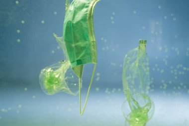 Suda kullanılan tıbbi maskenin yanında plastik torbalar ve fincanlar, ekoloji konsepti
