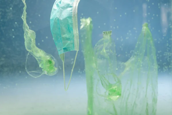 stock image plastic bags and cups near medical mask underwater, ecology concept