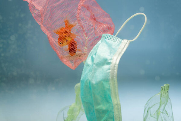 рыба в сети возле медицинской маски и пластиковый мусор в воде, экологическая концепция