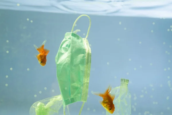 stock image plastic garbage and medical mask near goldfishes in water, ecology concept