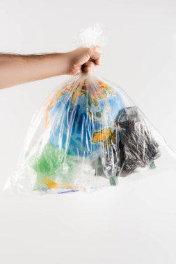 Çöplerle dolu plastik poşet tutan adamın kısmi görüntüsü gri, ekoloji kavramına izole edilmiş.