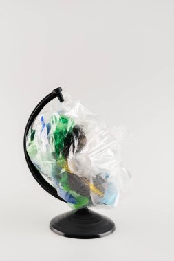 cellophane pack with plastic garbage on globe stand isolated on grey, ecology concept clipart