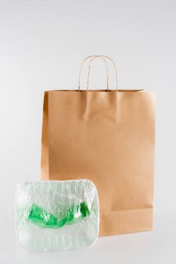 plastic plate and bottle packed in cellophane near paper bag on grey, ecology concept clipart
