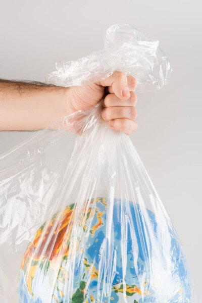 cropped view of man holding plastic bag with globe isolated on grey, ecology concept