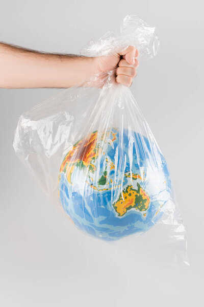 частичный вид человека, держащего целлофановый мешок с глобусом, изолированный на сером, экологическая концепция