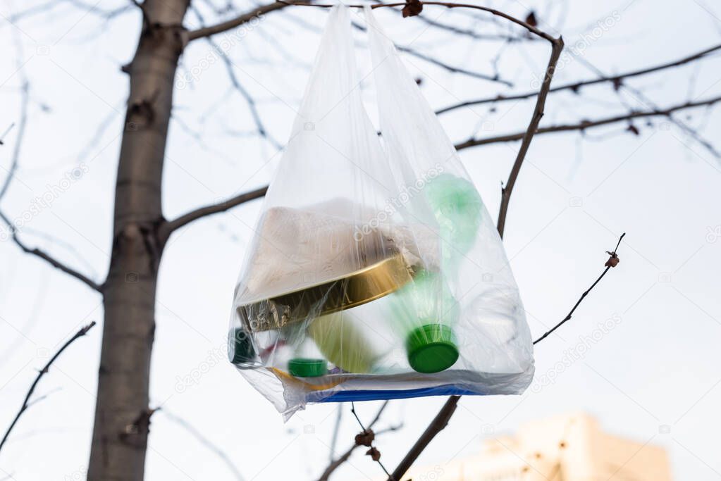 plastic bottles and tin in cellophane bag on tree, ecology concept
