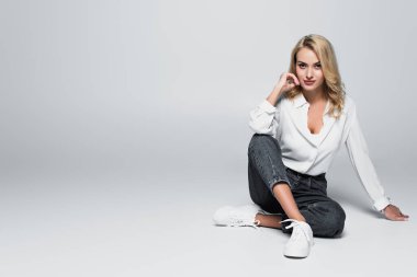 young, trendy woman holding hand near face while sitting on grey