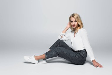 trendy, blonde woman looking at camera while sitting on grey