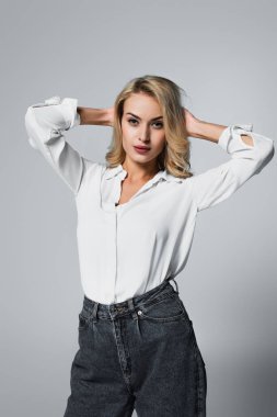 sensual woman in white shirt posing with hands behind head on grey