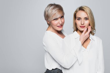 middle aged, stylish woman touching face of young daughter isolated on grey