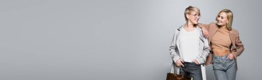 mature woman looking at stylish daughter isolated on grey, banner