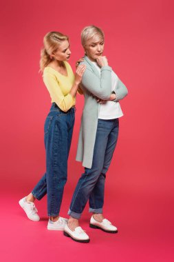 full length view of young woman touching shoulder of offended mother on pink