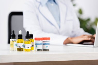 Tıbbi esrar şişeleri ve CBD harfleri bulanık arka planda doktorun yanındaki masada.