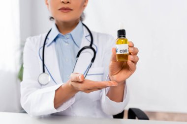 Afro-Amerikalı bir doktorun elindeki şişeyi CBD ile göstermesi. 