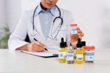 Elinde steteskop şişesi olan, üzerinde tıbbi kenevir yazıları olan ve panoya yazı yazan Afro-Amerikan doktorunun kısmi görüntüsü