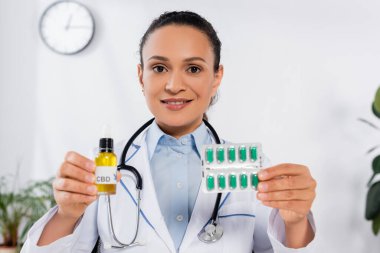 Steteskoplu neşeli Afrikalı Amerikalı doktor CBD şişesinin yanında kapsüllü su topladı.