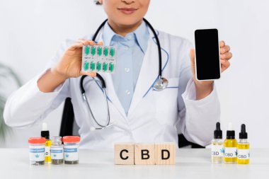 Afro-Amerikan doktorların kapsüllü su toplayan paketleri ve CBD küpleri ve şişelerinin yanında boş ekranlı akıllı telefonları var. 
